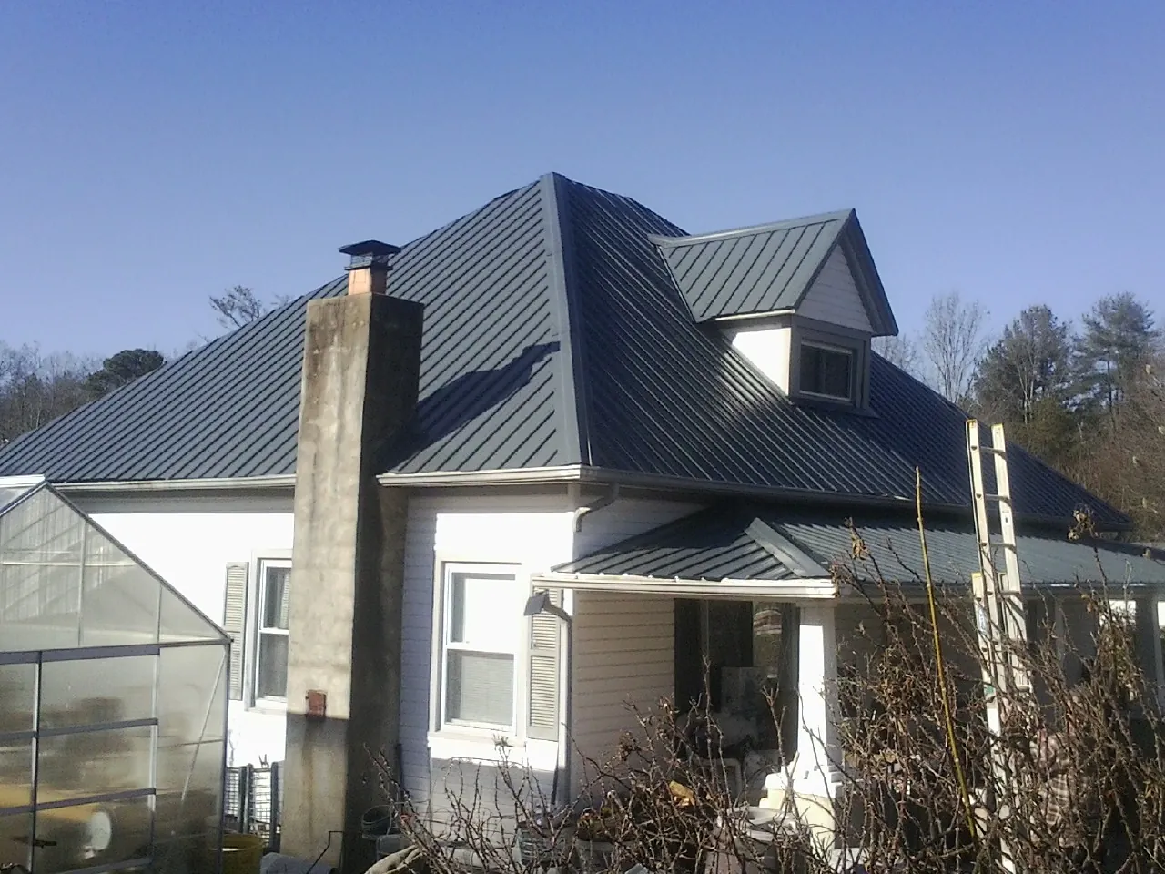 Dark blue standing seam metal roof on a white farmhouse with dormer — Slate & Tile Roof Repair by Roofing Brothers in Mount Ayr