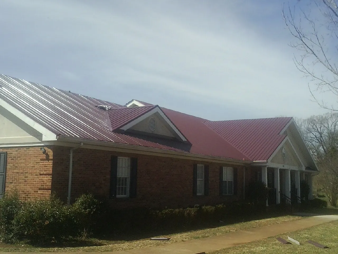 Red metal roof with gabled entries on a long brick building, from a Hail Damage Roof Repair job in Mount Ayr