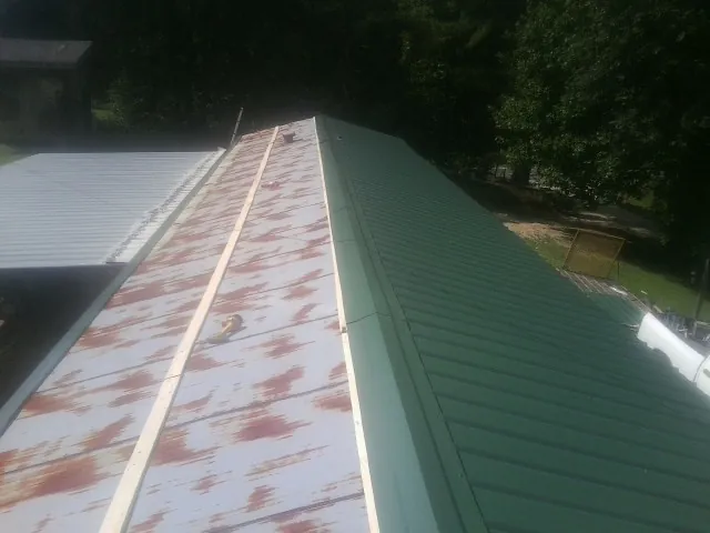 Old rusted panels beside newly installed green metal roofing — Wind Damage Roof Repair by Roofing Brothers in Mount Ayr