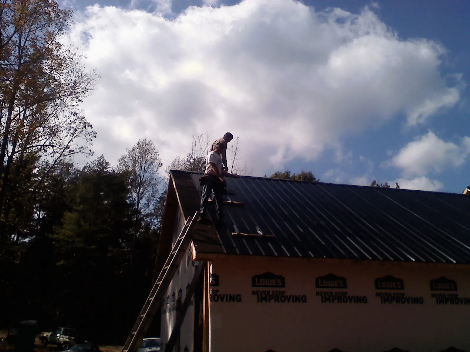 Roofer fastening dark metal panels high against a cloudy sky, from a Roof Inspection job in Mount Ayr