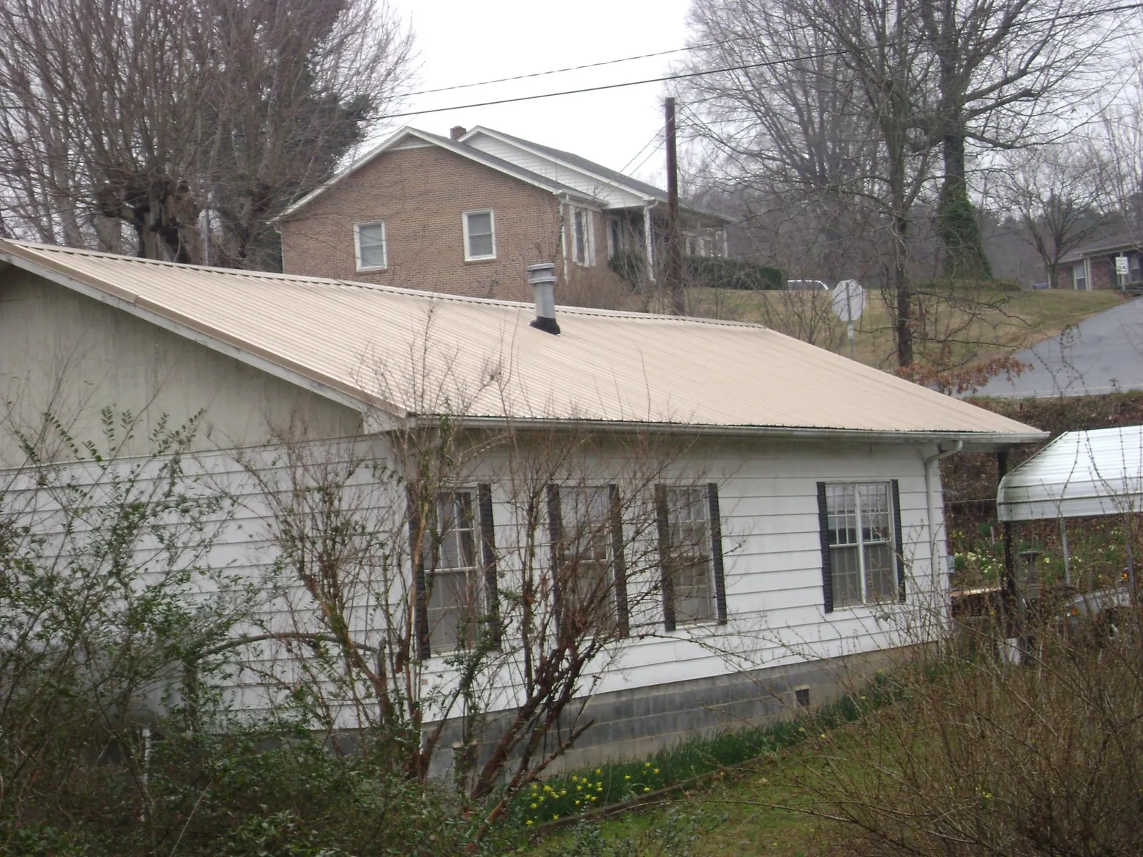 Tan metal roof on a white sided house set into a hillside — Commercial Roofing by Roofing Brothers in Mount Ayr