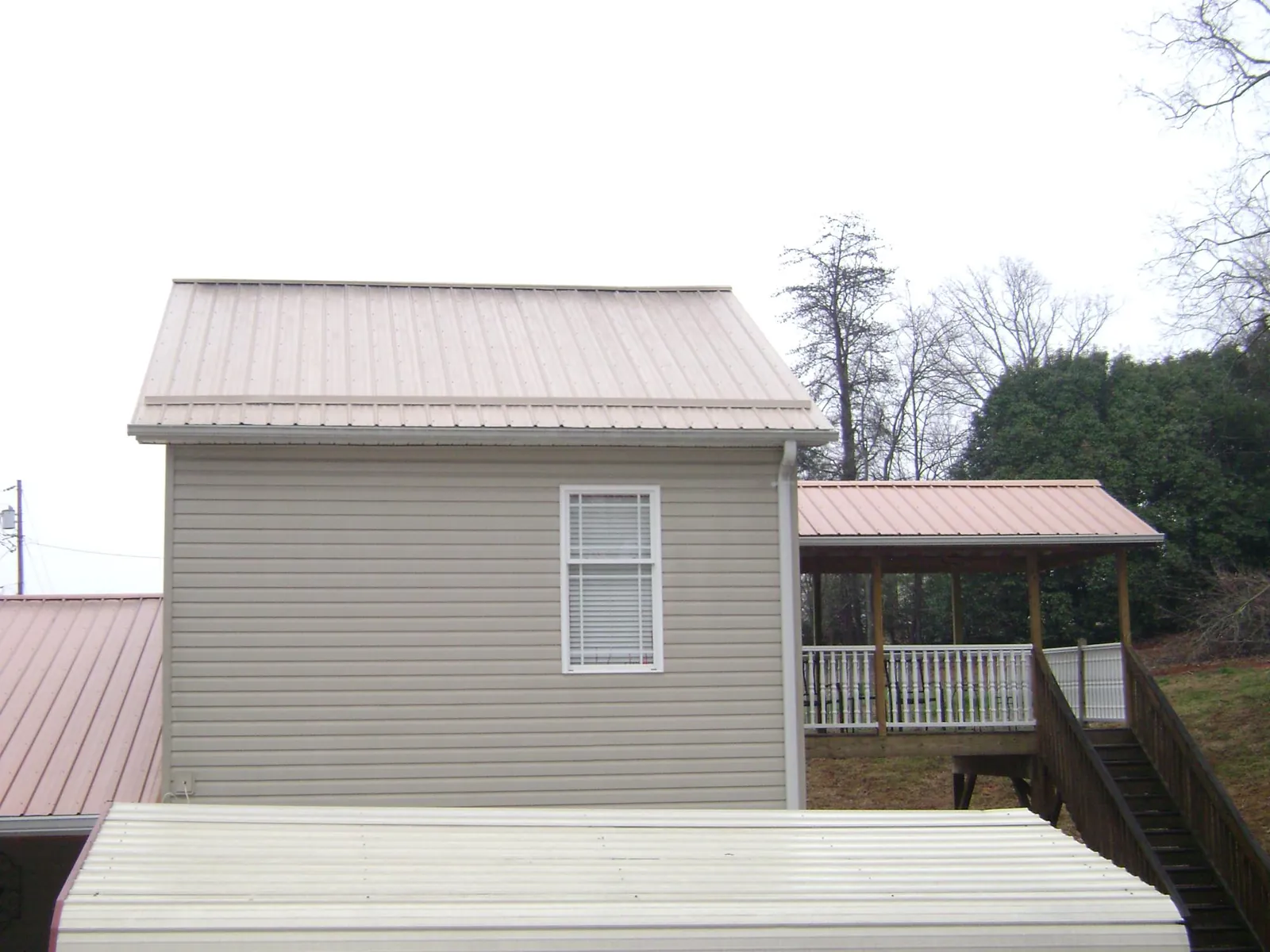 Tan metal roofs on a two story addition and attached porch, from a Roof Replacement job in Mount Ayr